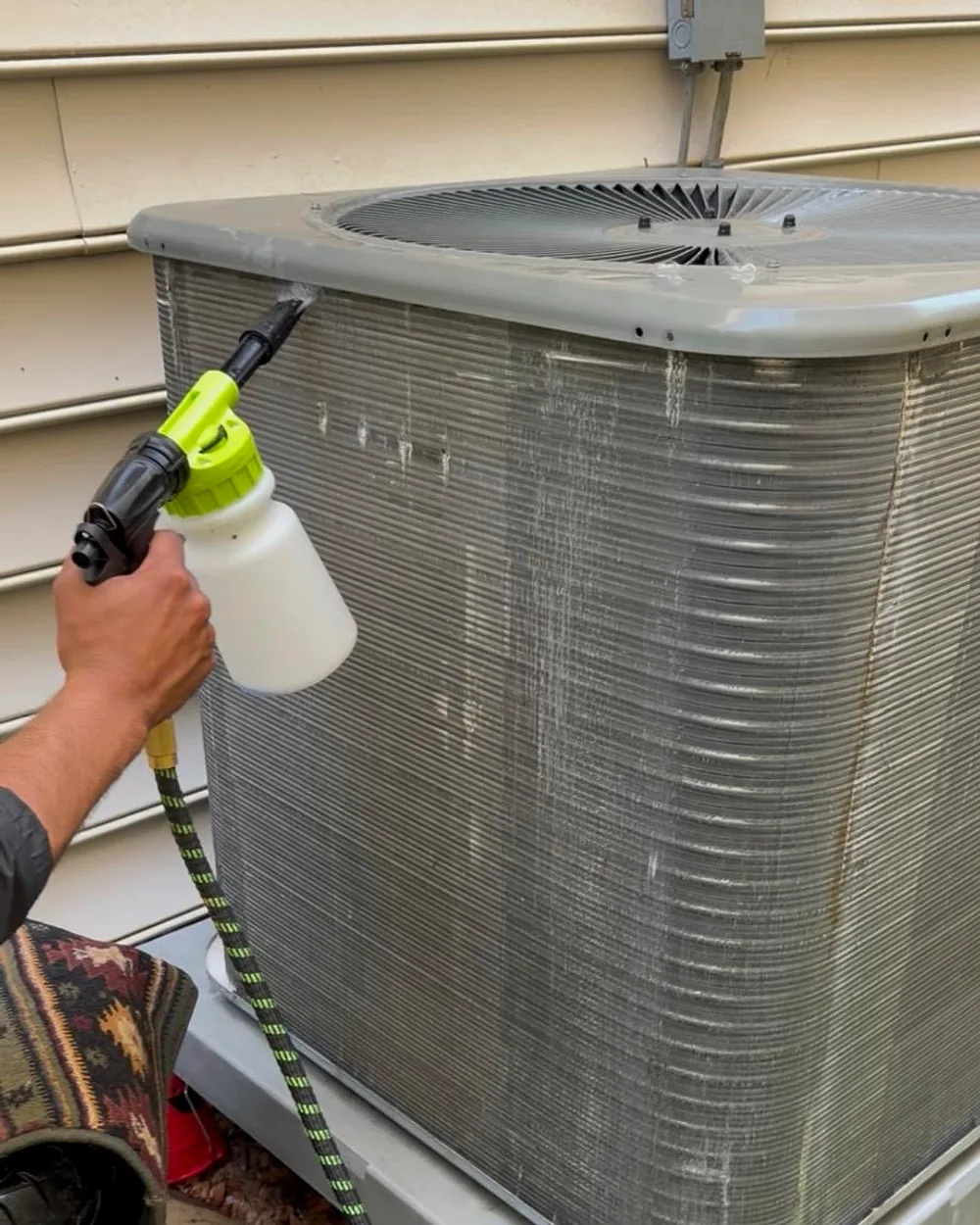 Technician cleaning an AC condenser coil during a maintenance tune-up